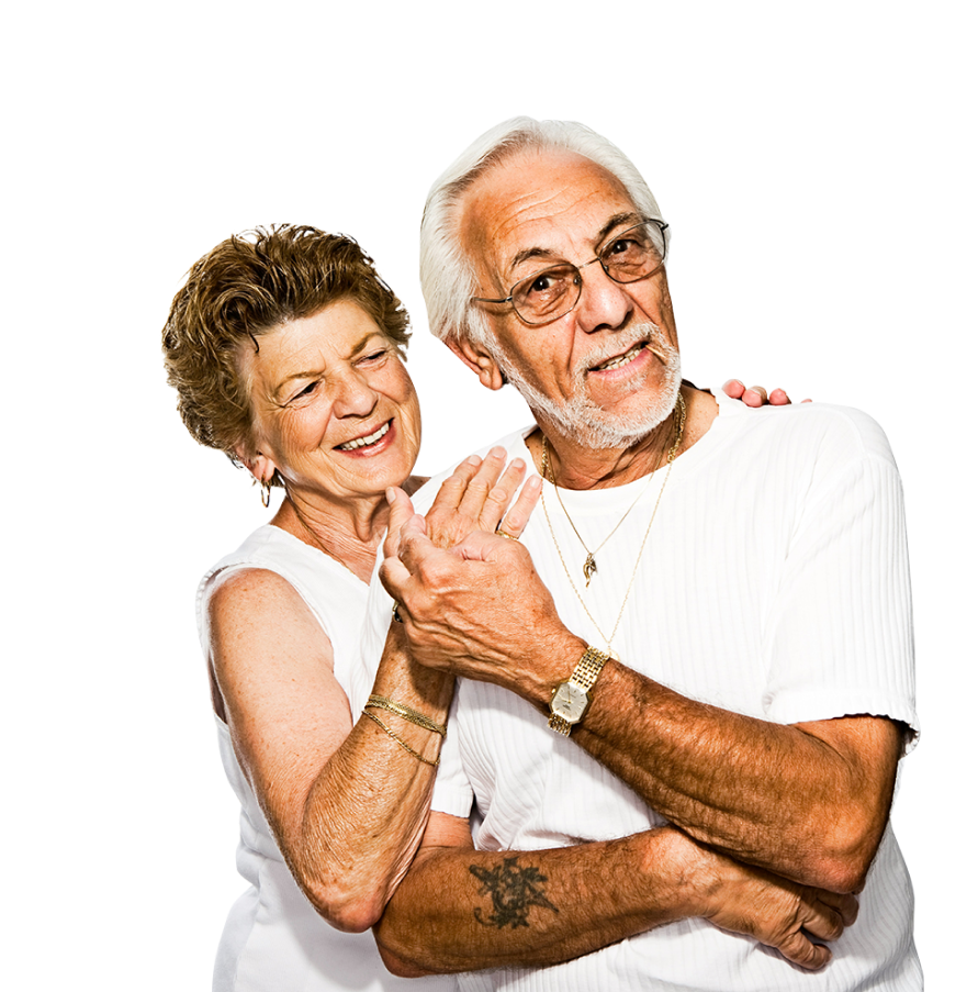 An elderly couple stands close together, smiling warmly in the heart of central Florida. The woman has short, curly hair and wears a sleeveless white top. She places her arm affectionately around the shoulders of the man, who has white hair, glasses, and a white shirt.