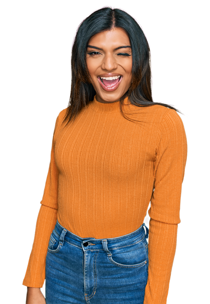 A person with long dark hair, wearing an orange long-sleeve ribbed shirt and blue jeans, stands against a maroon background. They are smiling broadly and winking with one eye.