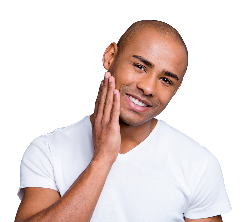 A smiling person with short hair in a white t-shirt, touching their cheek with their right hand. The background is plain and neutral.
