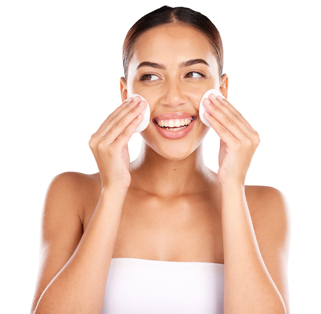 A woman with dark hair is smiling and using two cotton pads to cleanse her face. She is wearing a white strapless top and has a fresh and happy expression. The background is plain white.
